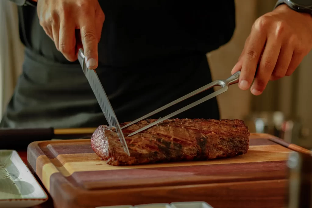 Slicing Cooked Steak on Wood Board by chef