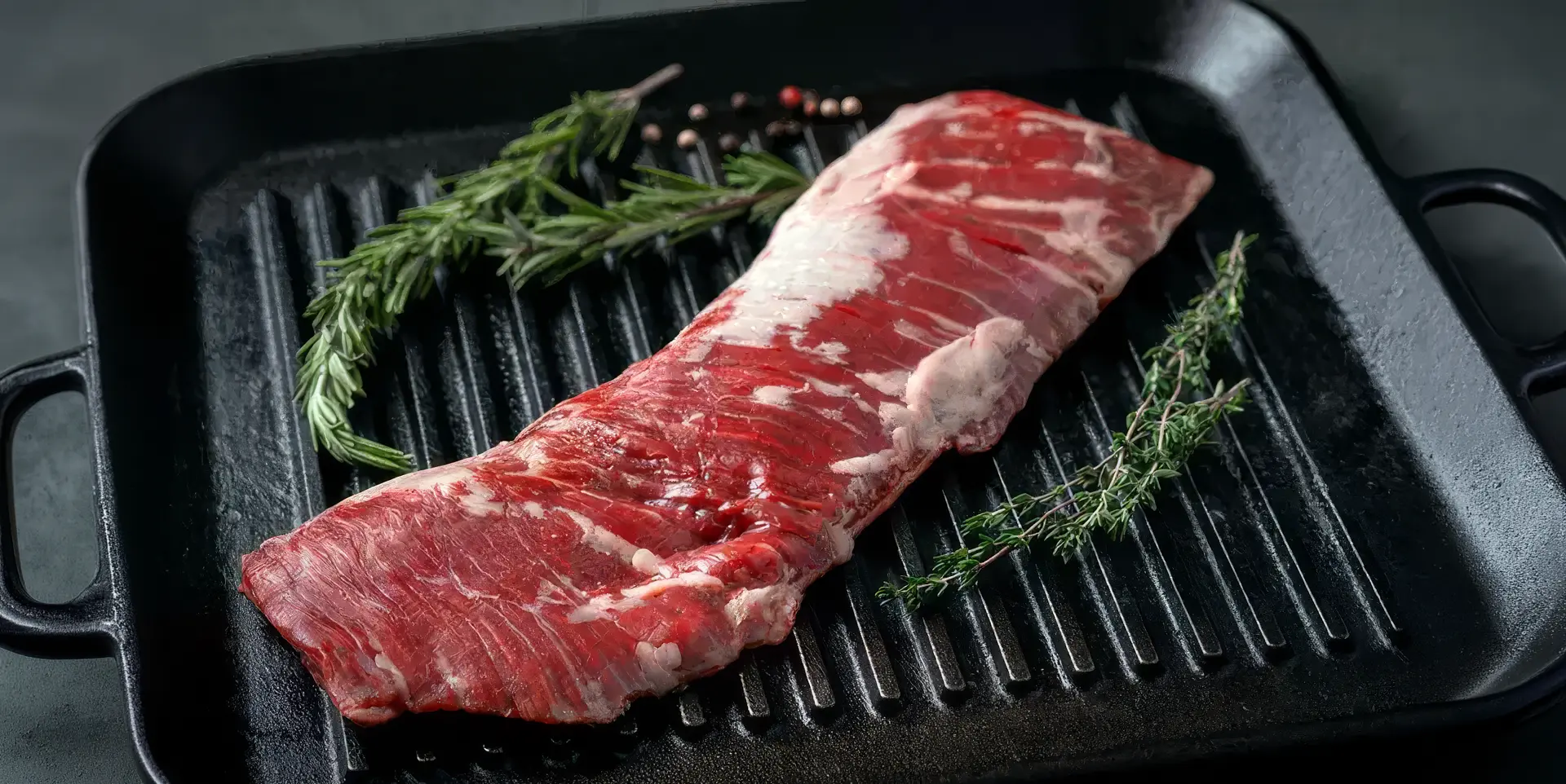 Grass-Fed Ontario Beef Skirt Steak, known for it's marbling and quick cooking properties, presented on a pan sear plate with herbs and peppercorns in preparation for cooking