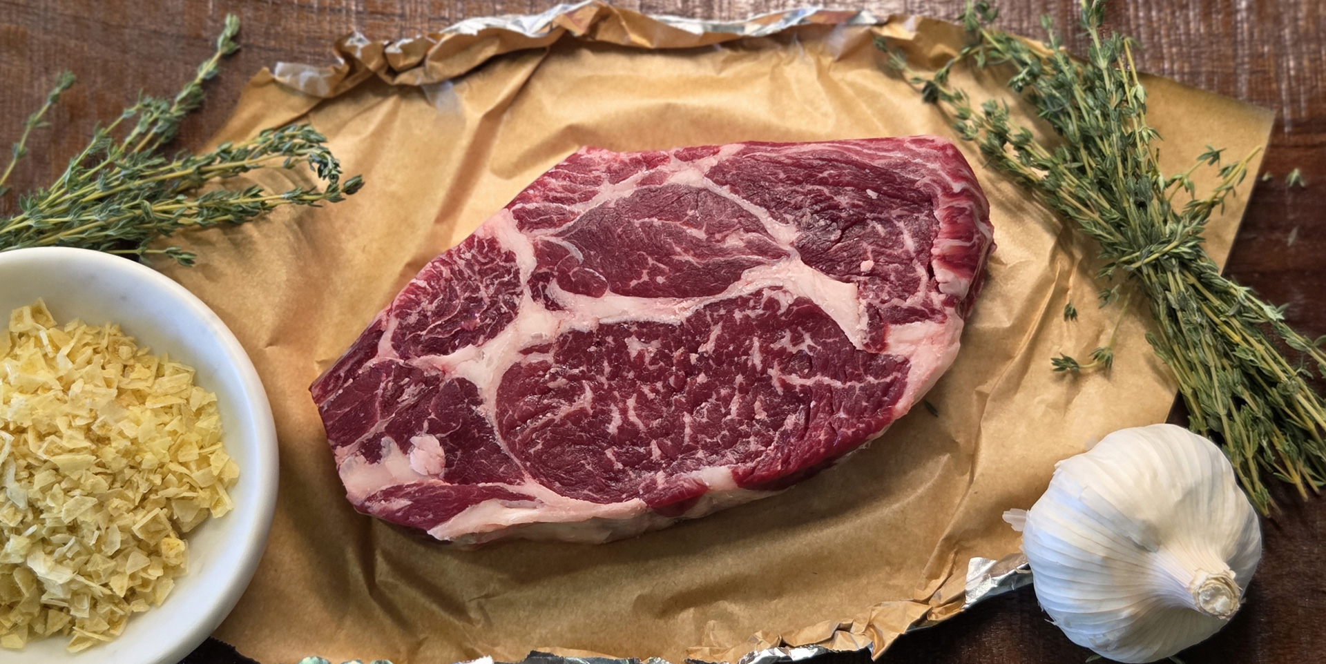 Rib-Steak, rich and marbled on a table with thyme, garlic and preparation herbs